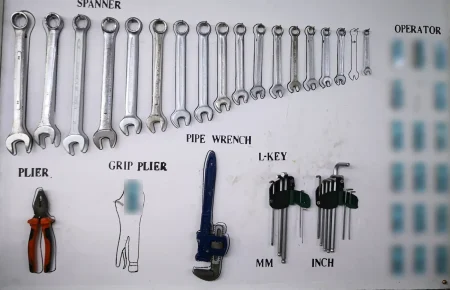A white workshop shadow board with outlined spanners, pliers, a pipe wrench and hex keys, where an empty outline marks a tool that is missing
