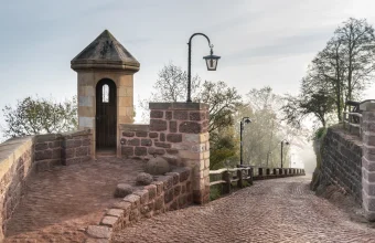 A stone sentry box on a castle wall beside a lamp post and a cobblestone path in morning mist at Wartburg Castle