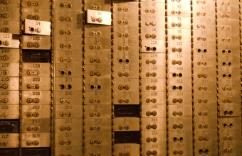 A brass wall of numbered bank safe deposit boxes, each with a pair of keyholes