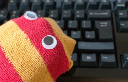 A red and yellow striped sock puppet with googly eyes resting on a black computer keyboard