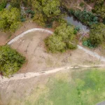 Aerial view of a worn dirt desire line cutting straight across a hillside beside a curving paved trail