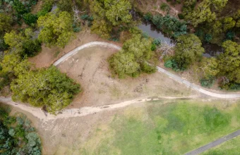 Aerial view of a worn dirt desire line cutting straight across a hillside beside a curving paved trail