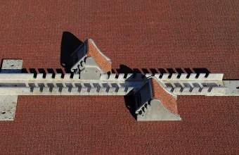 Overhead view of an athletics starting block, with two angled foot plates on a slotted metal rail, lying on a red running track