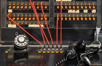 Close-up of a vintage Western Electric manual telephone switchboard with orange lamps, red patch cords plugged into jacks, a rotary dial and a black handset