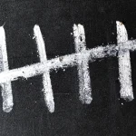 Four white chalk strokes crossed by a diagonal fifth stroke on a black chalkboard, a tally of five