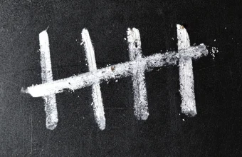 Four white chalk strokes crossed by a diagonal fifth stroke on a black chalkboard, a tally of five