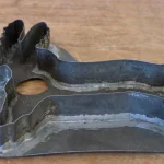 An old tin cookie cutter with a fixed animal-shaped outline lying on a wooden table