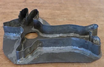 An old tin cookie cutter with a fixed animal-shaped outline lying on a wooden table