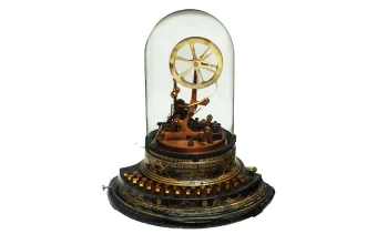 An antique Edison stock ticker under a glass dome, a machine that printed a continuous stream of text sent from far away