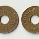 Two brass Gothenburg ferry tokens, front and back, each with a round hole in the middle, on a plain light background
