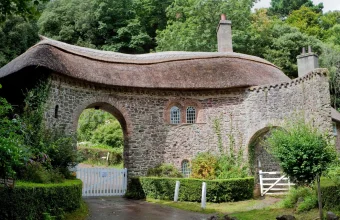 A stone gatehouse with a thatched roof and a white toll gate across a road in Somerset, England