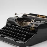 LibreOffice’s “No AI” Turns a Product Promise Into a Contribution Policy, and Its Git Log Holds 48 Disclosed LLM Commits Where The Register Cited Three A black 1935 Olympia Simplex portable typewriter with gold lettering, photographed against a plain light grey background