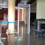 An empty security checkpoint in a building lobby with a walk-through metal detector and an X-ray baggage scanner on a polished floor
