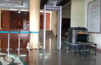 An empty security checkpoint in a building lobby with a walk-through metal detector and an X-ray baggage scanner on a polished floor