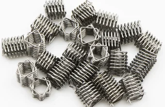 A pile of small stainless steel coil springs lying on a white background